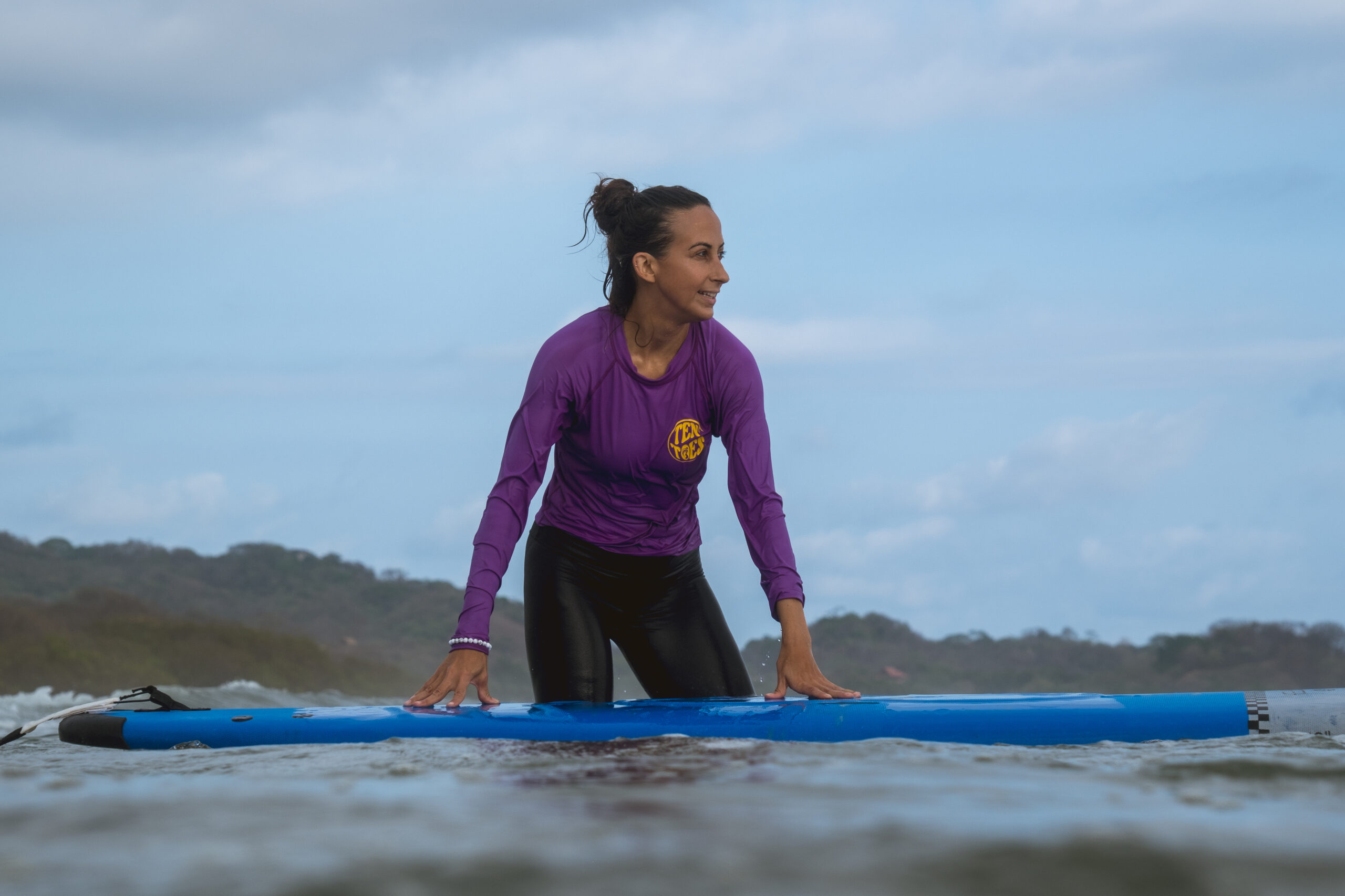 Sofia Estrella, standing in the ocean with a determined expression, prepares to get on her surfboard, ready to overcome her fear and embrace the challenge at the 2024 NUSHU Surf Retreat.